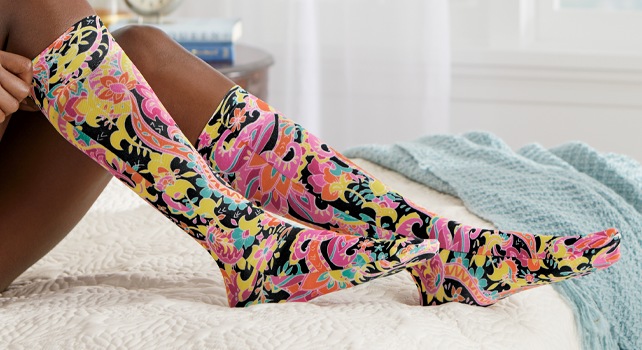 Woman on bed pulling on bright floral compression socks