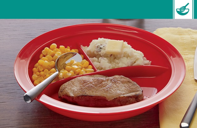 Red partition plate with a spoon, meat, corn and mashed potatoes