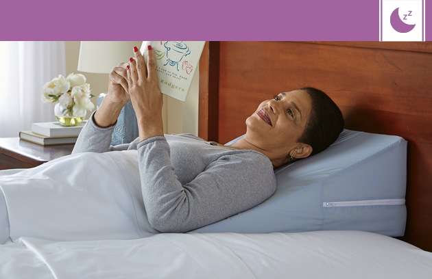 Woman lying in bed resting on a bed wedge while reading a book